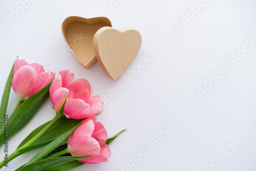 top view of pink tulips near craft heart-shaped gift box on white.