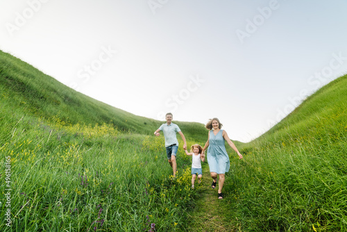 Happy young family spending time together, running on nature, on vacation, outdoors. Mom, dad, and daughter walk in the green grass. The concept of family holiday.