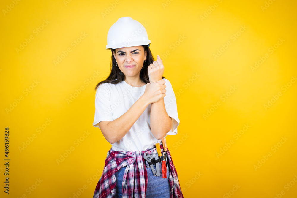 Young caucasian woman wearing hardhat and builder clothes over isolated yellow background suffering pain on hands and fingers, arthritis inflammation Young caucasian woman wearing hardhat and builder clothes over isolated yellow background suffering pain on hands and fingers, arthritis inflammation