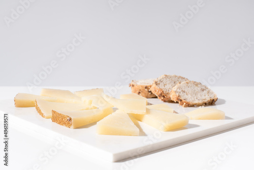 Trozos de queso manchego de oveja curado con tostadas de pan crujiente sobre una mesa blanca. Tapas españolas photo