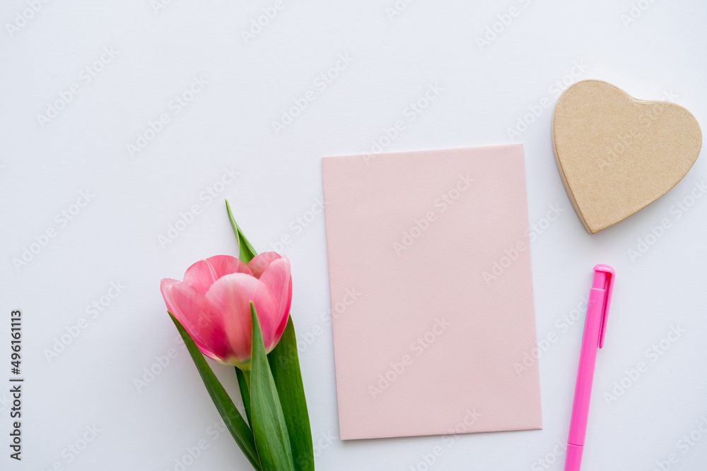 top view of pink tulip near pastel envelope, pen and craft heart-shaped paper on white. top view of pink tulip near pastel envelope, pen and craft heart-shaped paper on white.