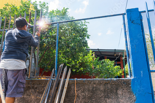 Blue collar worker from latin america seen from the back welding a metal fence