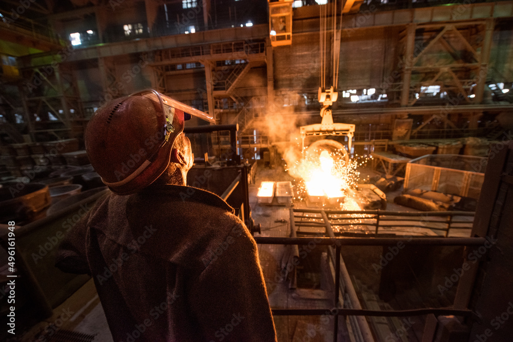 Steelworker when pouring liquid metal from tanks in the molds at a steel mill. Steelworker when pouring liquid metal from tanks in the molds at a steel mill.