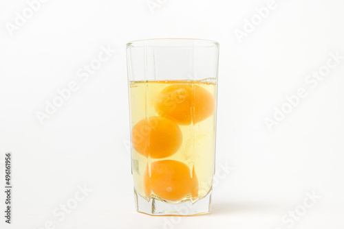 Broken raw chicken eggs in a glass on a white background. Chicken egg yolk. Drinking raw chicken eggs