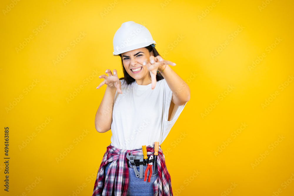 Young caucasian woman wearing hardhat and builder clothes over isolated yellow background smiling funny doing claw gesture as cat, aggressive and sexy expression Young caucasian woman wearing hardhat and builder clothes over isolated yellow background smiling funny doing claw gesture as cat, aggressive and sexy expression