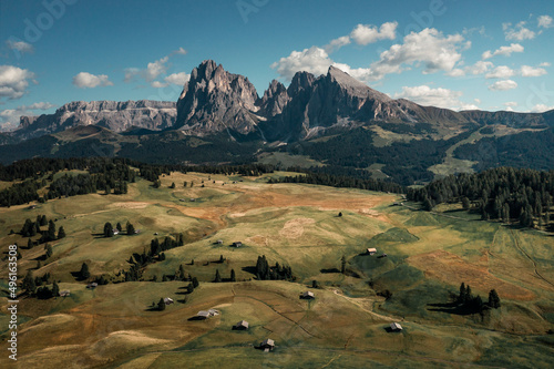 Meadows with wooden cabins at Alpe di Siusi during summer with view to mountains of Plattkofel and Langkofel in the Dolomite Alps from above in South Tyrol, Italy.