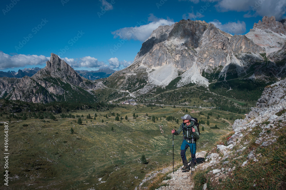 Man hiking along trail to Croda Negra mountain summit at Passo di Falzarego during sunny blue sky day in the Dolomite Alps, South Tyrol Italy.