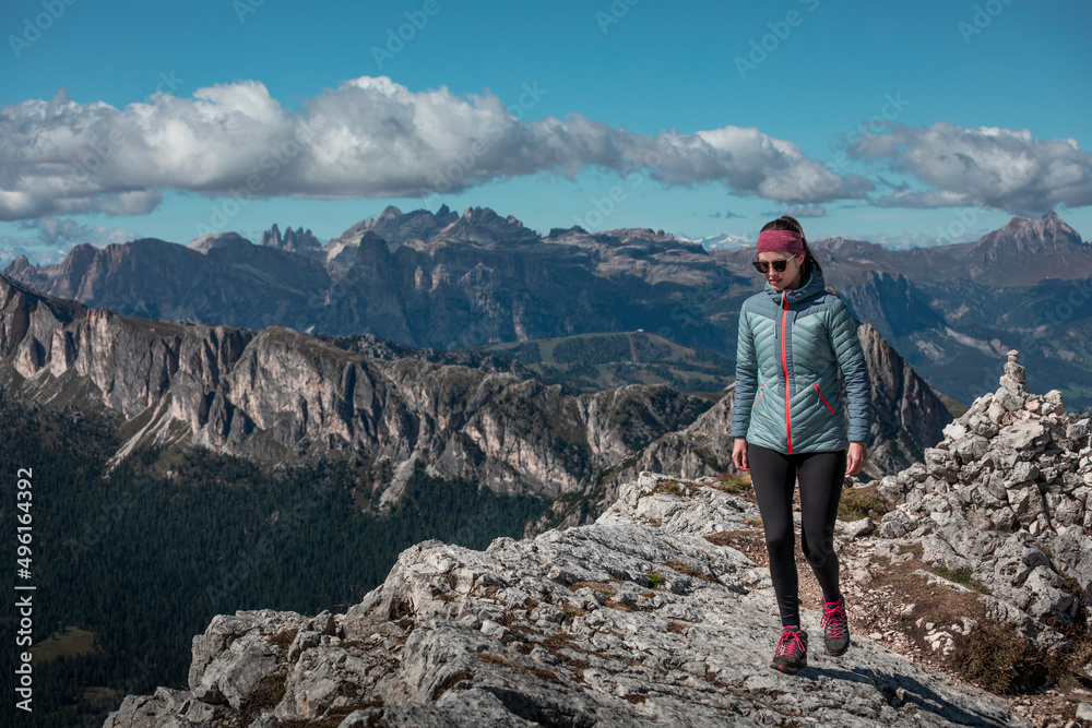 Woman hiking along trail to Croda Negra mountain summit at Passo di Falzarego during sunny blue sky day in the Dolomite Alps, South Tyrol Italy.