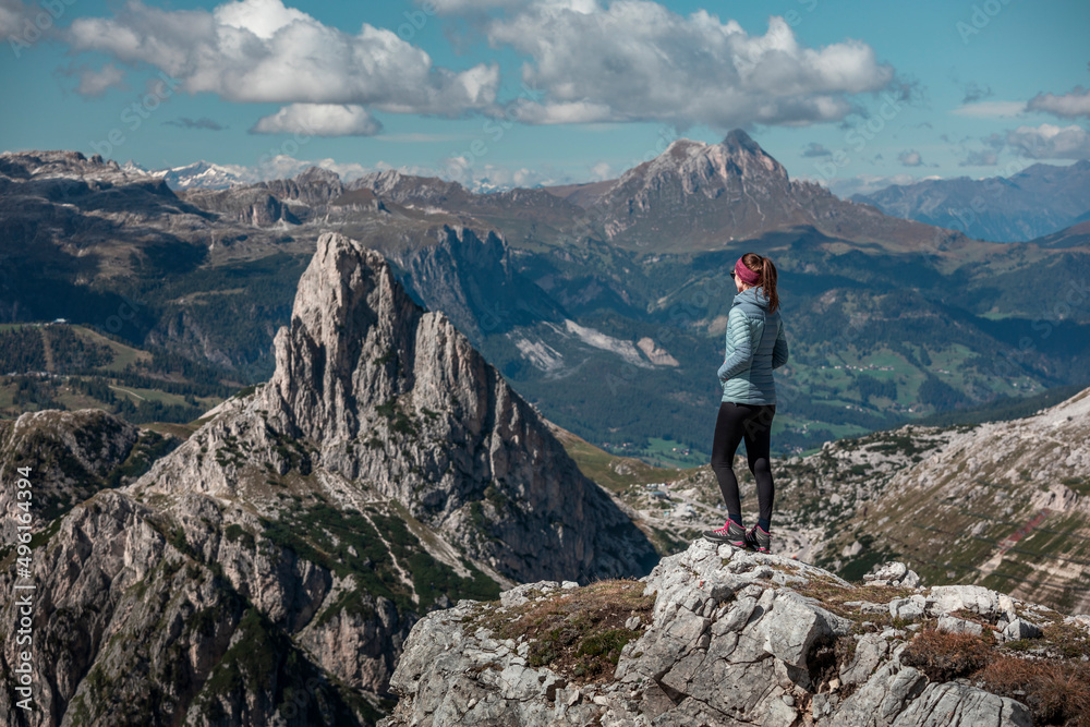 Woman on summit of Croda Negra looking to mountain summit of Hexenstein at Passo di Falzarego during sunny blue sky day in the Dolomite Alps, South Tyrol Italy.