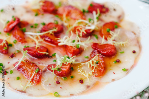 Sea bass carpaccio with baked strawberries and citrus dressing. Dish in the restaurant, strawberry menu. Summer light dish for gourmets. Closeup