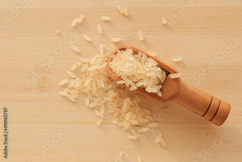 Rice scattering in a wooden spoon on a light board. The product is dietary, the benefits of proper nutrition. Cereals in nutrition - concept.