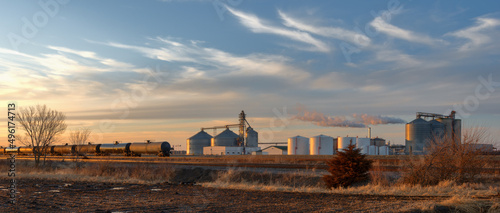 Farmland producing ethanol for the oil and gas industry.  Railroad tankers cars lined up near a ethanol plant at sunset.