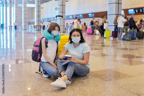 Mother and daughter child in protective medical masks at the airport with luggage