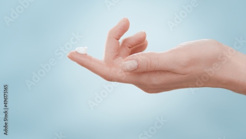Female hand with a drop of skin care cream on forefinger against blue background | Skin care cream commercial concept