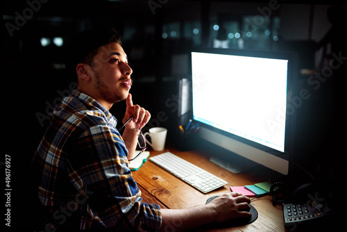 Great ideas can come at any time. Shot of a young male designer deep in thought whhile working on his computer late at night.