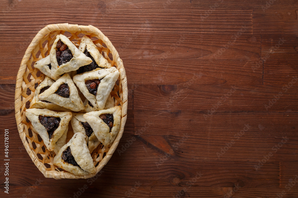Gomentash with poppy seeds and prunes freshly baked for the Purim holiday on a wooden table in a wicker bread basket.copy space. Gomentash with poppy seeds and prunes freshly baked for the Purim holiday on a wooden table in a wicker bread basket.copy space.