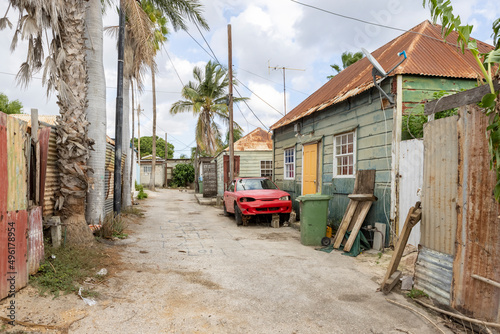 Fototapeta Naklejka Na Ścianę i Meble -  Side street with small weathered house and a broken red car in the front in the suburbs of Willemstad, Curacao