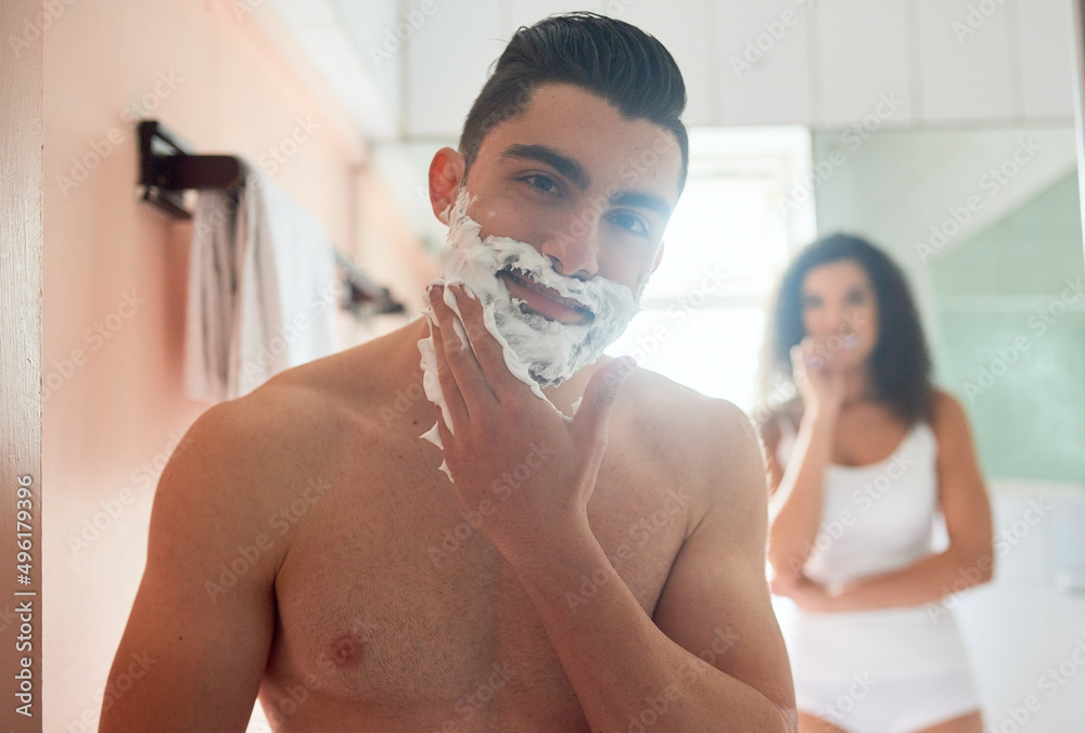 Time to get rid of this hair. Shot of a handsome young man shaving while his girlfriend brushes her teeth in the bathroom.