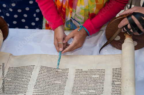 A young woman celebrating her Bat Mitzvah reads from the Torah using a colorful yad or pointer to guide her through the Hebrew text. photo