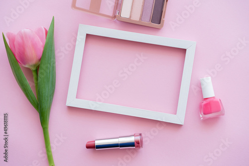 top view of decorative cosmetics near blooming tulip and frame on pink.