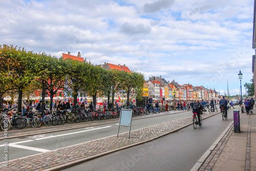 Bicyclists ride past parked bicycles along the Nyhavn Canal in the historic, touristic district of Copenhagen Denmark.