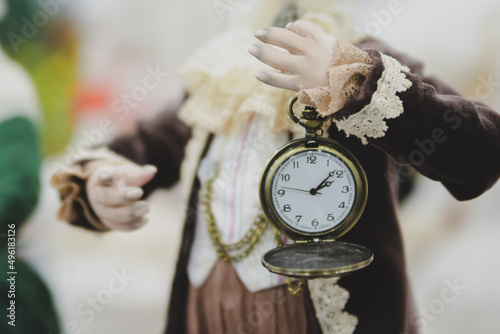 The doll is holding an old mechanical watch with a flip cover.