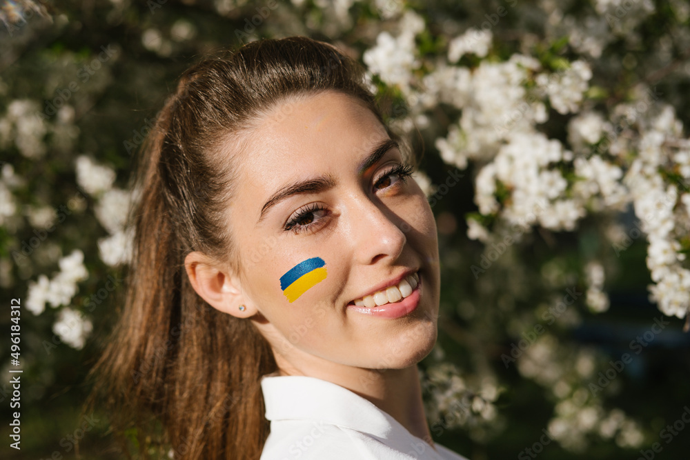 Outdoor portrait of ukrainian woman with blue and yellow ukrainian flag on her cheek on cherry blossom nature. Symbol of freedom and independence of Ukraine. Stop the war. Hope and Faith Outdoor portrait of ukrainian woman with blue and yellow ukrainian flag on her cheek on cherry blossom nature. Symbol of freedom and independence of Ukraine. Stop the war. Hope and Faith