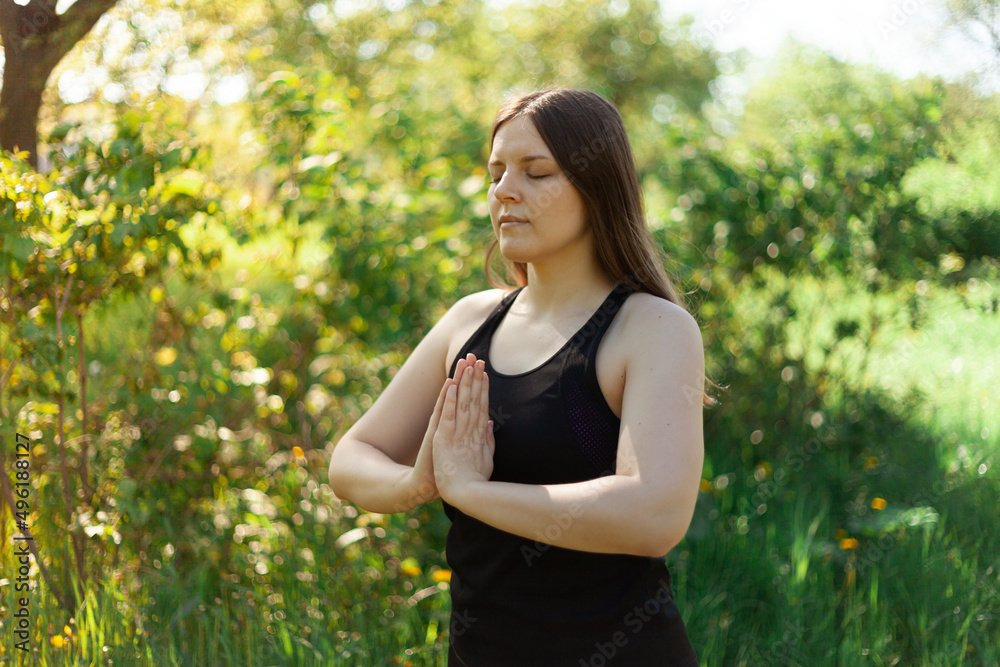 The brunette folded her hands in a namaste gesture during a yoga class in a city park. Summer, green grass, healthy lifestyle during the coronavirus pandemic The brunette folded her hands in a namaste gesture during a yoga class in a city park. Summer, green grass, healthy lifestyle during the coronavirus pandemic