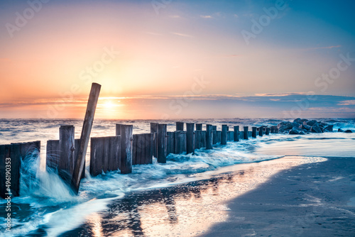 Seascape of wooden breakwater pier at sunrise with ocean tide