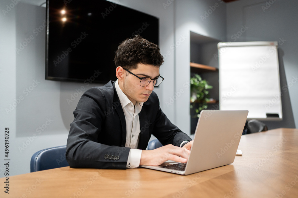 A manager with glasses in a suit uses a laptop computer works in an office coworking space A manager with glasses in a suit uses a laptop computer works in an office coworking space