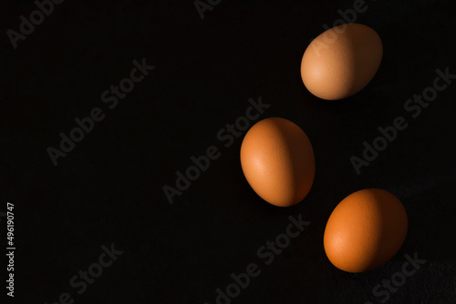 Natural home product. Fresh brown eggs with hard shadows on a dark background. Minimalism. Top view. Copy space.