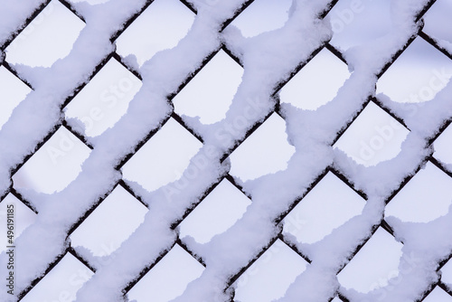 Mesh fence covered in snow. Adhering snow on the fence after a blizzard. Snow drifts.