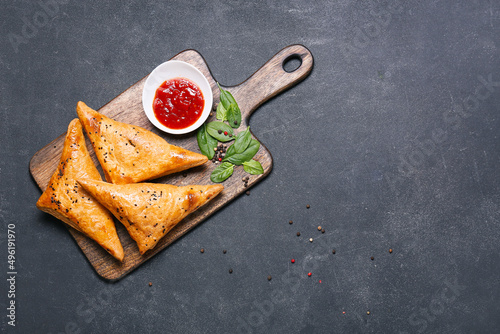 Board with tasty Uzbek samsa and tomato sauce on dark background photo