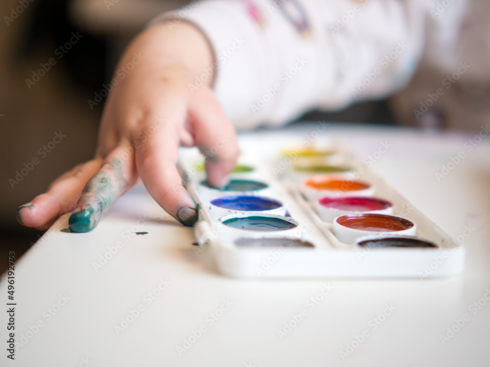 The girl sits at the table and draws with her fingers in the sketchbook. Children's creativity. Children's hobbies. The girl sits at the table and draws with her fingers in the sketchbook. Children's creativity. Children's hobbies.