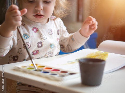 A 2-year-old girl sits at a table and learns to draw with multi-colored watercolors. Children's creativity. Children's hobbies.