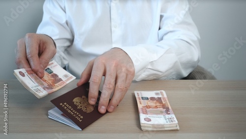 A close-up of an unrecognizable businessman counting cash banknotes in five thousand Russian rubles and investing money in a Russian passport. 