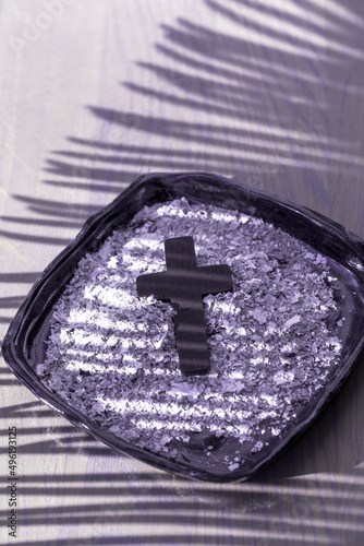 A Christian cross with palm leaf shadow on ashes background. Lent Season, Holy Week and Good Friday concept. Flat lay. Copy space.