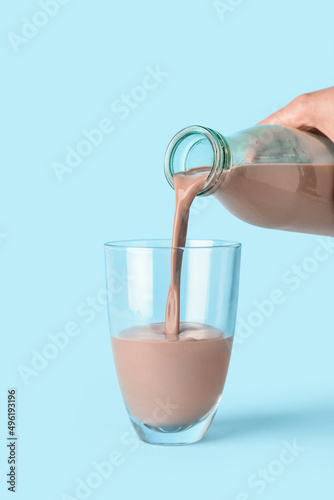 Pouring of delicious chocolate milk from bottle into glass on color background
