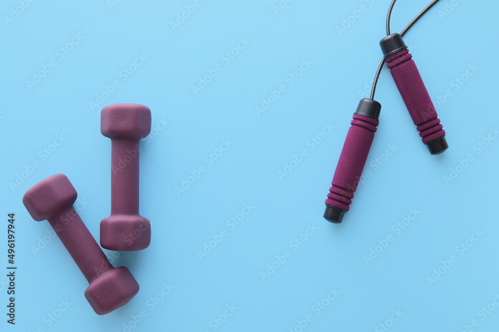 Stylish dumbbells and skipping rope on blue background Stylish dumbbells and skipping rope on blue background