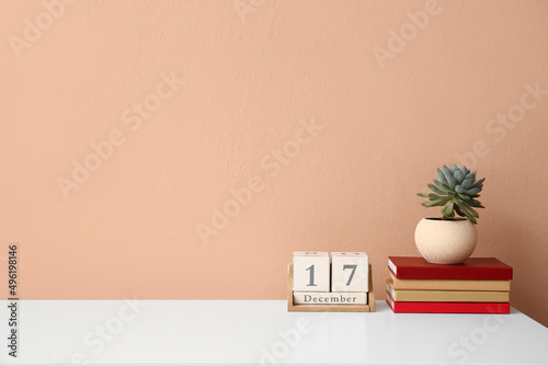 Stack of books, houseplant and cube calendar on table near color wall