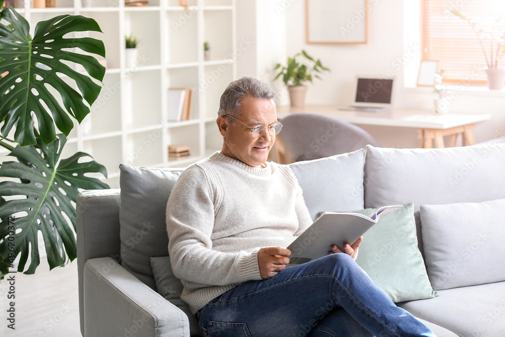 Senior man in eyeglasses reading magazine on sofa at home Senior man in eyeglasses reading magazine on sofa at home