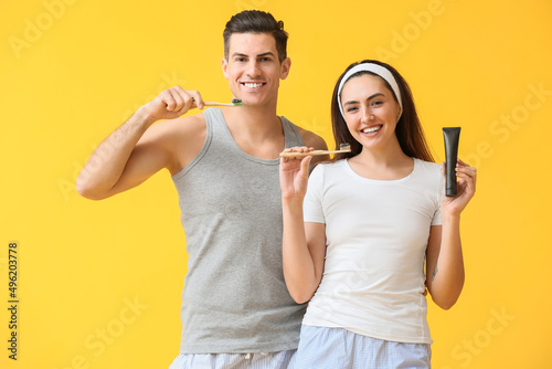 Young couple with activated charcoal tooth paste and brushes on yellow background