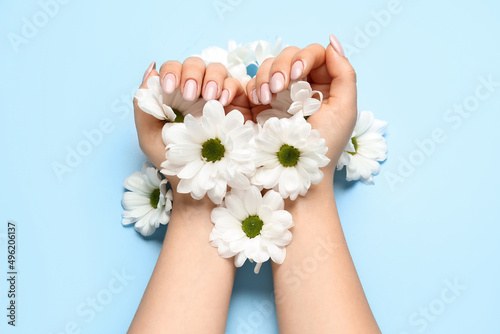 Female hands with beautiful manicure and daisy flowers on blue background
