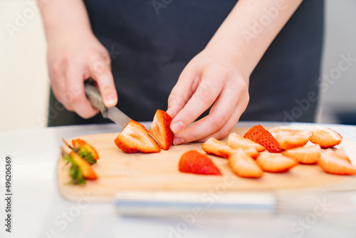 strawberries are cut into pieces on a wooden cutting board to decorate desserts.