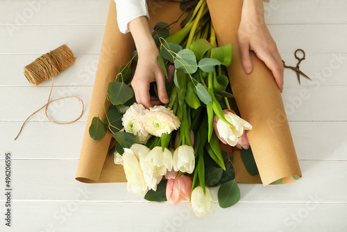 Female florist wrapping in craft paper beautiful bouquet at light wooden background