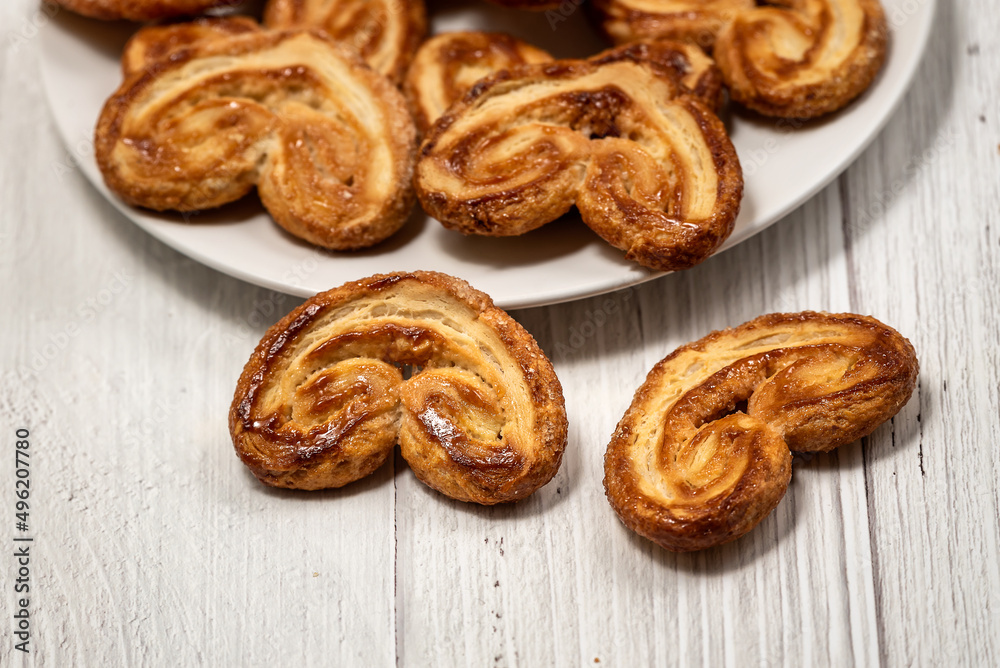Palmier puff pastry biscuits in white plate on a white painted wooden table Palmier puff pastry biscuits in white plate on a white painted wooden table
