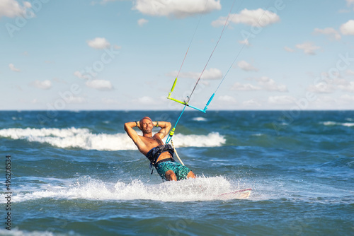 Portrait young adult caucasian fit male person enjoy riding kite surf board making fun trick stunt bright sunny day against blue sky at sea ocean shore. Watersport adrenaline fun adventure acitivity