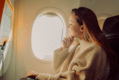 A beautiful girl sits in an airplane at the window and looks at the view. Tourist travel