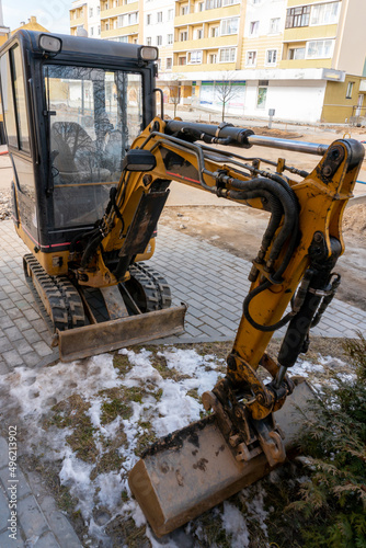 Mini excavator on the construction site. Replacement of paving slabs and repair of roads in the city. Crawler excavator with a bucket while digging a trench for laying new pipes