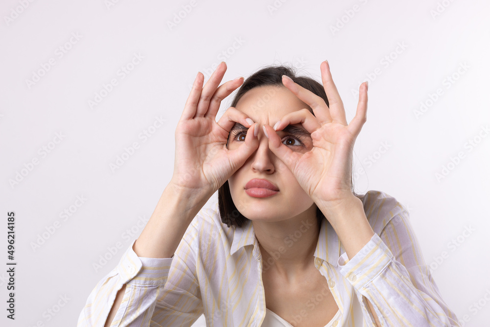 Close up portrait of attractive quirky young woman making binoculars with hands showing ok gesture on white studio background. Close up portrait of attractive quirky young woman making binoculars with hands showing ok gesture on white studio background.